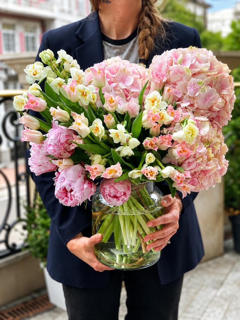 Los Angeles florist holding a luxury spring bouquet with pink hydrangeas, peonies, tulips, and white flowers in a glass vase.