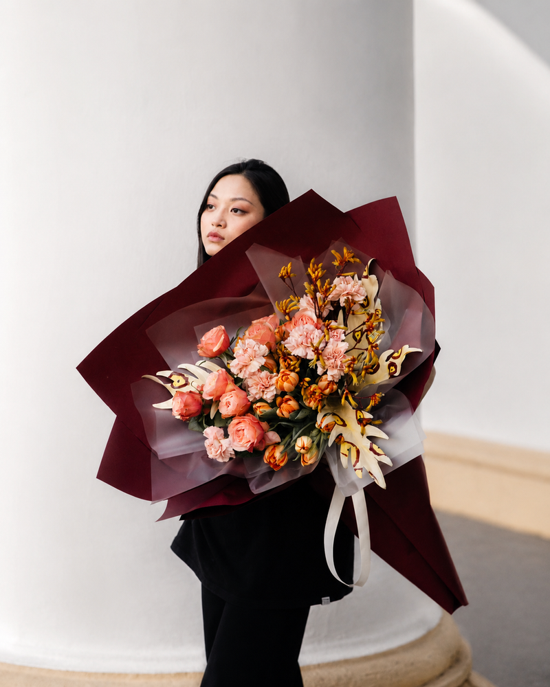 Luxury Los Angeles florist arrangement with peach, blush, and cream flowers in dramatic burgundy wrapping