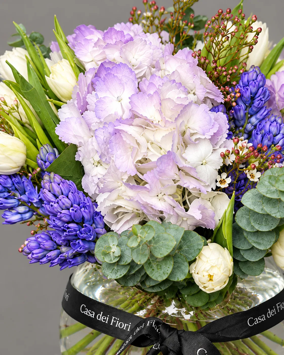 Purple Hydrangeas, Blue Hyacinths and White Tulips in Glass Vase by Casa Dei Fiori
