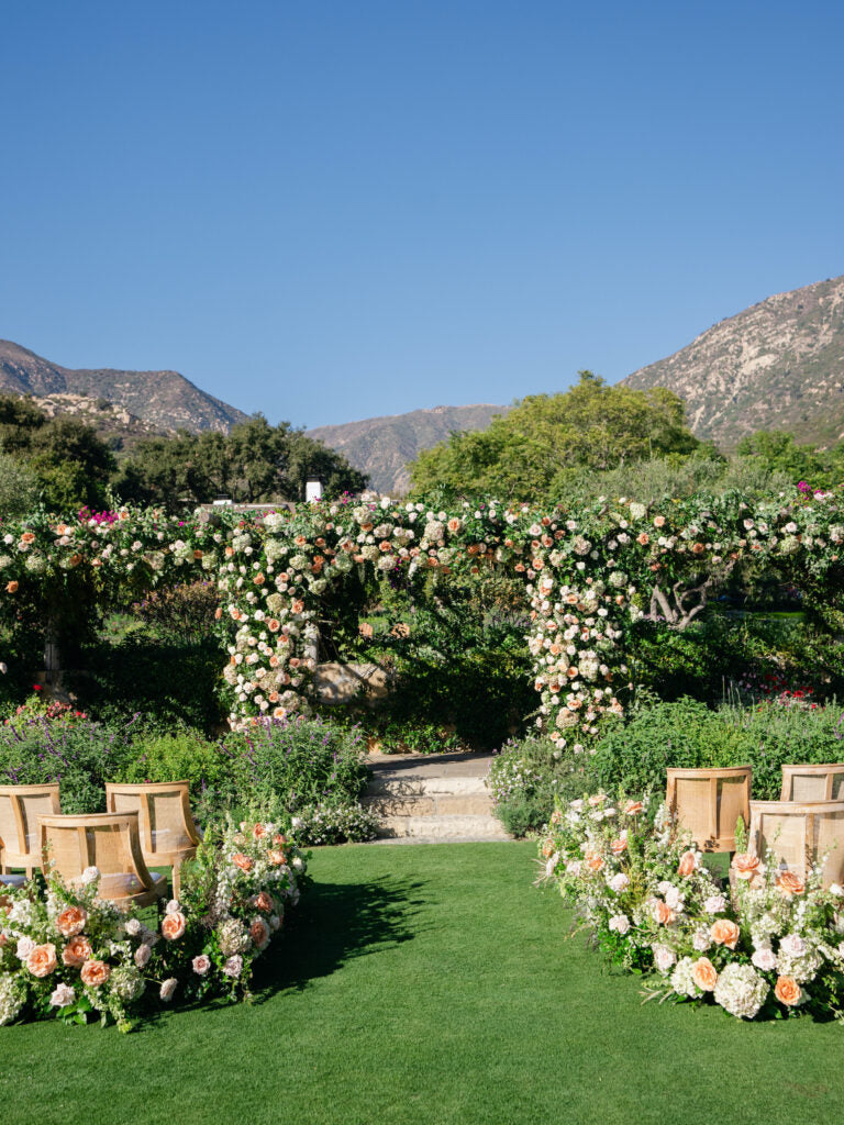 Romantic garden wedding ceremony with a custom floral arch and aisle arrangements